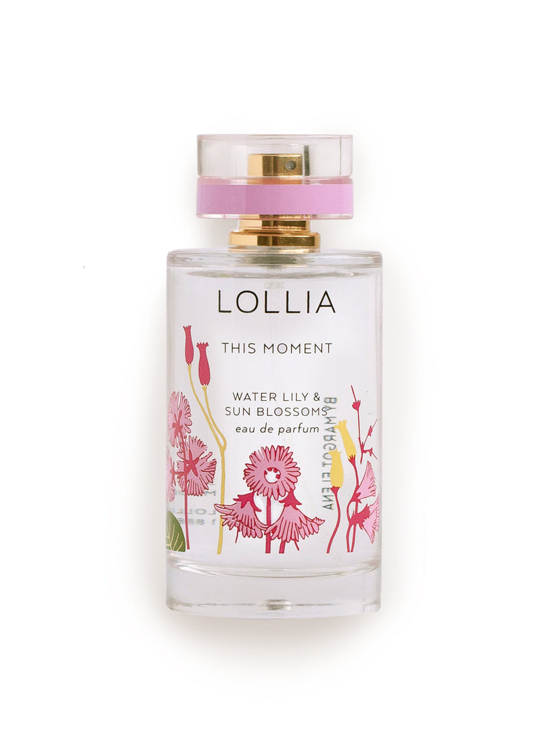 Transparent perfume bottle with floral designs and a pink label, marked "Margot Elena Lollia This Moment Eau de Parfum water lily & honey amber" on a white background.