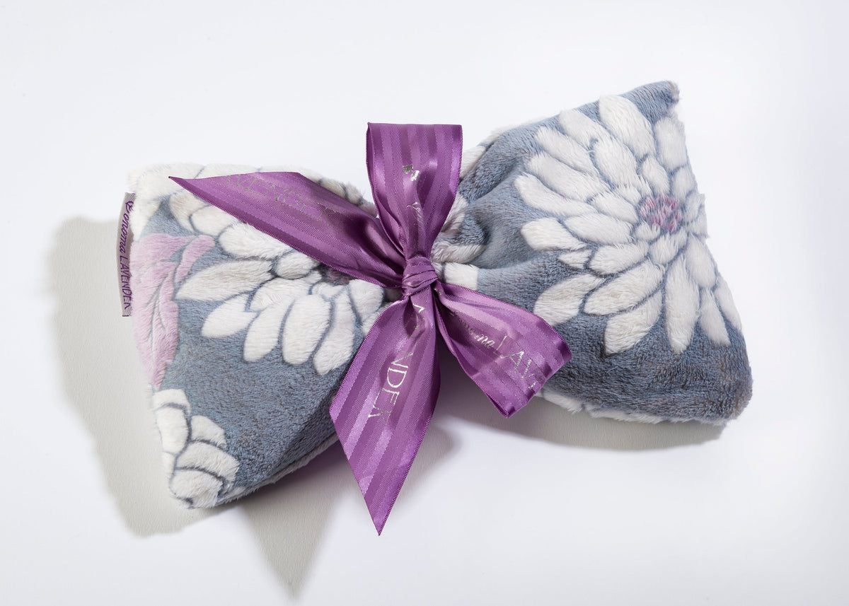 A floral patterned, soft fabric Sonoma Lavender Ibiza spa mask tied with a satin purple ribbon, presented on a plain light background. The mask appears gently textured and plush.
