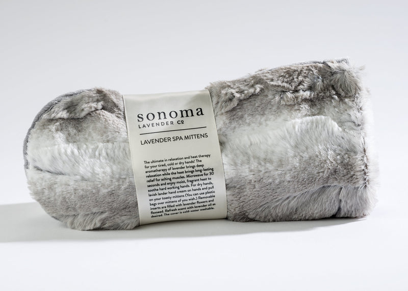A pair of Sonoma Lavender Angora Platinum Spa Mittens with plush, white and gray faux fur on a white background, featuring a label with product information.