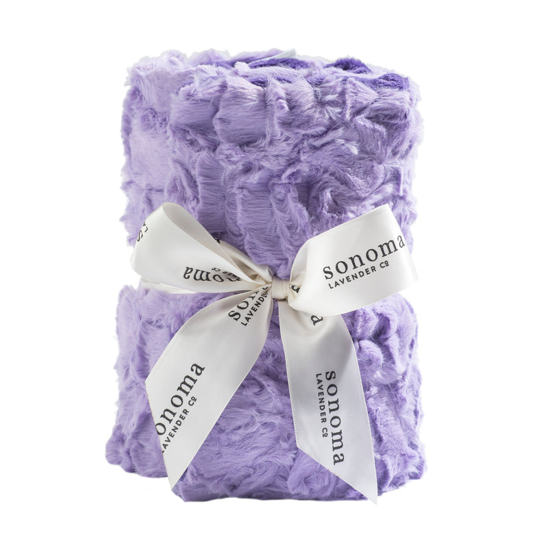 A plush lavender-colored Sonoma Lavender Bellflower Rose Heat Wrap tied with a white ribbon printed with "Sonoma Lavender" in cursive, isolated on a white background.