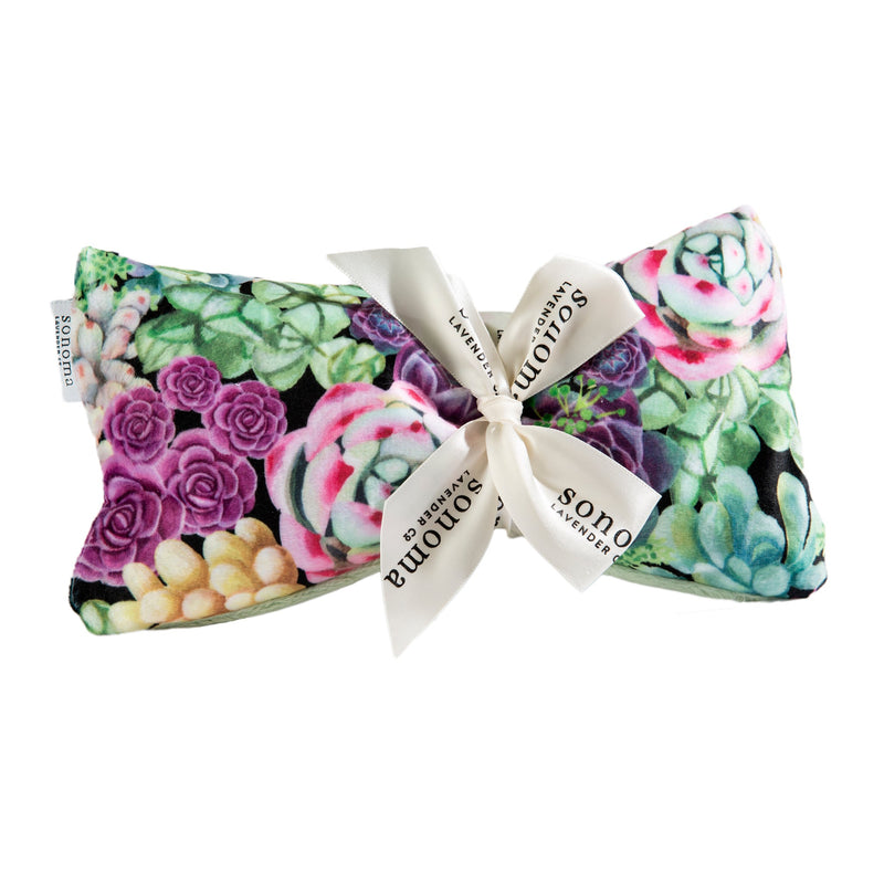 A Sonoma Lavender Succulents Spa Mask with a satin bow, featuring soothing words printed on the ribbon. Ideal for relaxation and heat therapy.