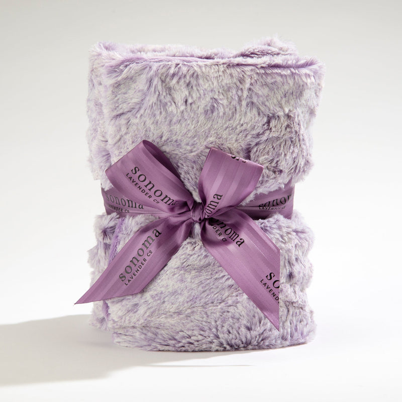 A plush, lavender-colored Sonoma Lavender Aster Heather Heat Wrap neatly folded and tied with a purple ribbon printed with the word "sonoma" multiple times. The background is plain white, emphasizing the heat wrap’s texture and color.