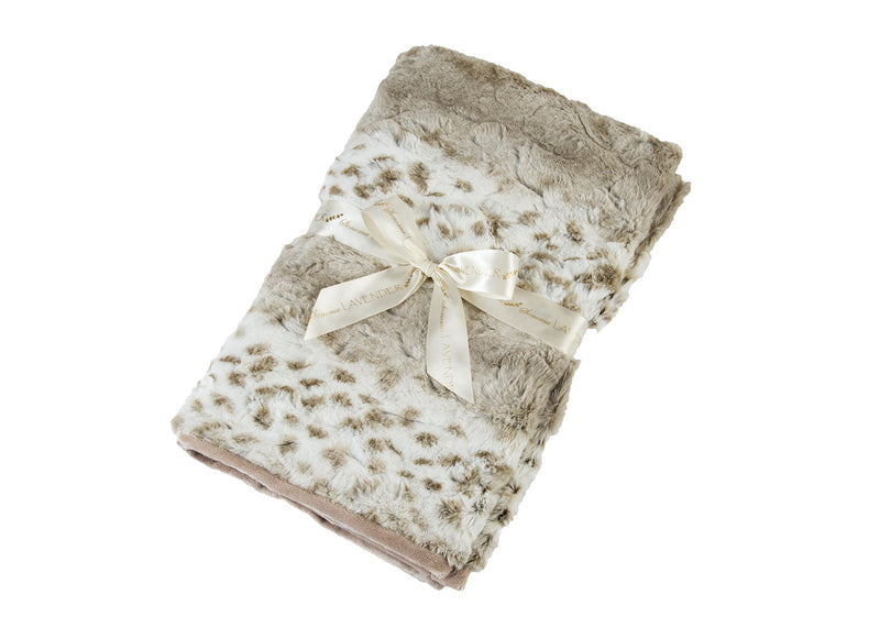 A soft, plush beige Sonoma Lavender Arctic Circle Spa Blankie tied with an elegant ivory ribbon, isolated on a white background. The ribbon features the word "luxurious" printed on it.