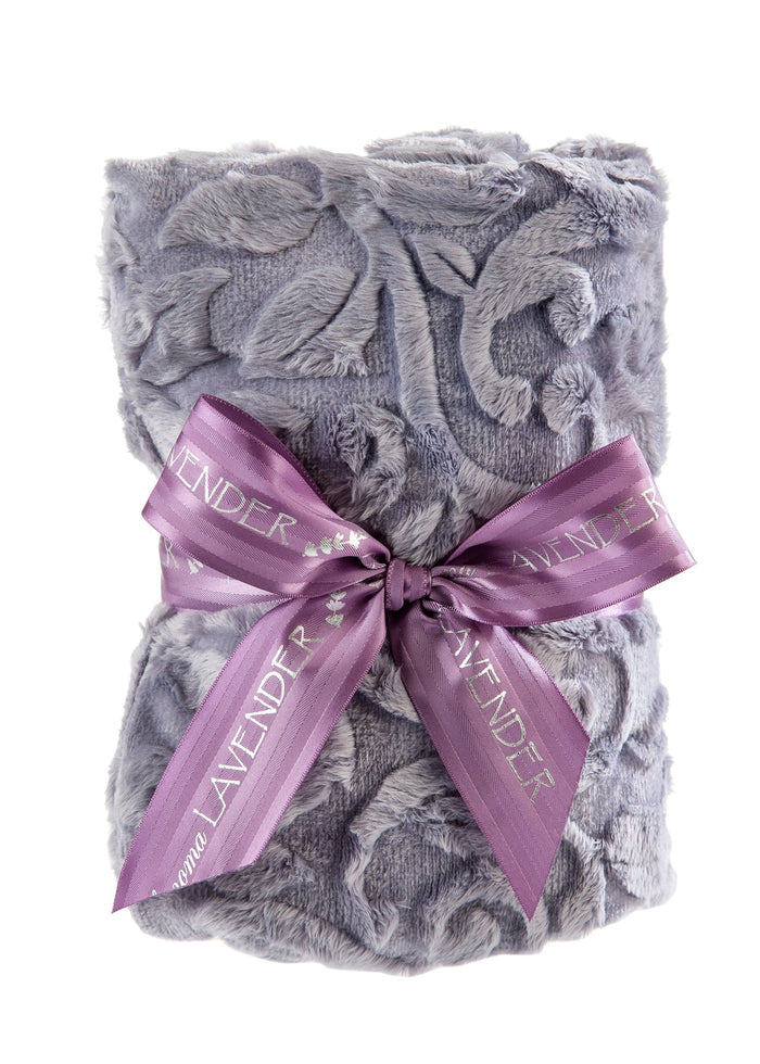 The Sonoma Lavender Platinum Vine Heat Wrap, by Sonoma Lavender, is a textured gray throw blanket with an ornate floral pattern, rolled and tied with a purple "LAVENDER" ribbon and subtly infused with lavender flowers for therapeutic warmth.