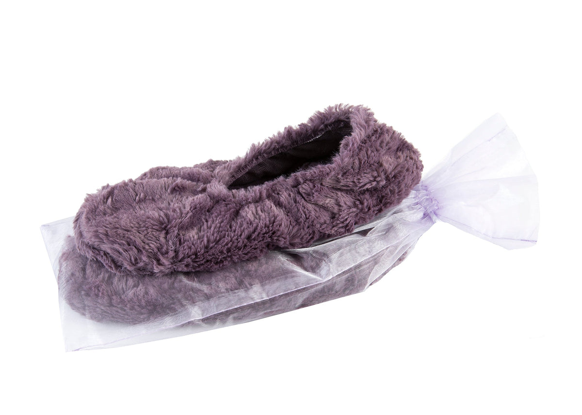 A soft, purple fuzzy slipper with Sonoma Lavender Grapemist Cuddle Heatable Footies nestled in a translucent, white drawstring bag against a white background.