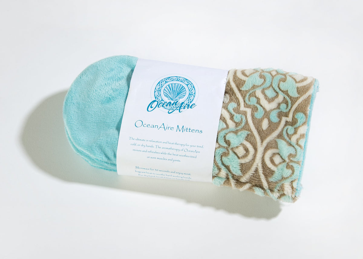 A pair of plush, teal and tan patterned Sonoma Lavender Spa Mittens with a product tag reading "Sonoma OceanAire Le Mer mittens" against a white background.