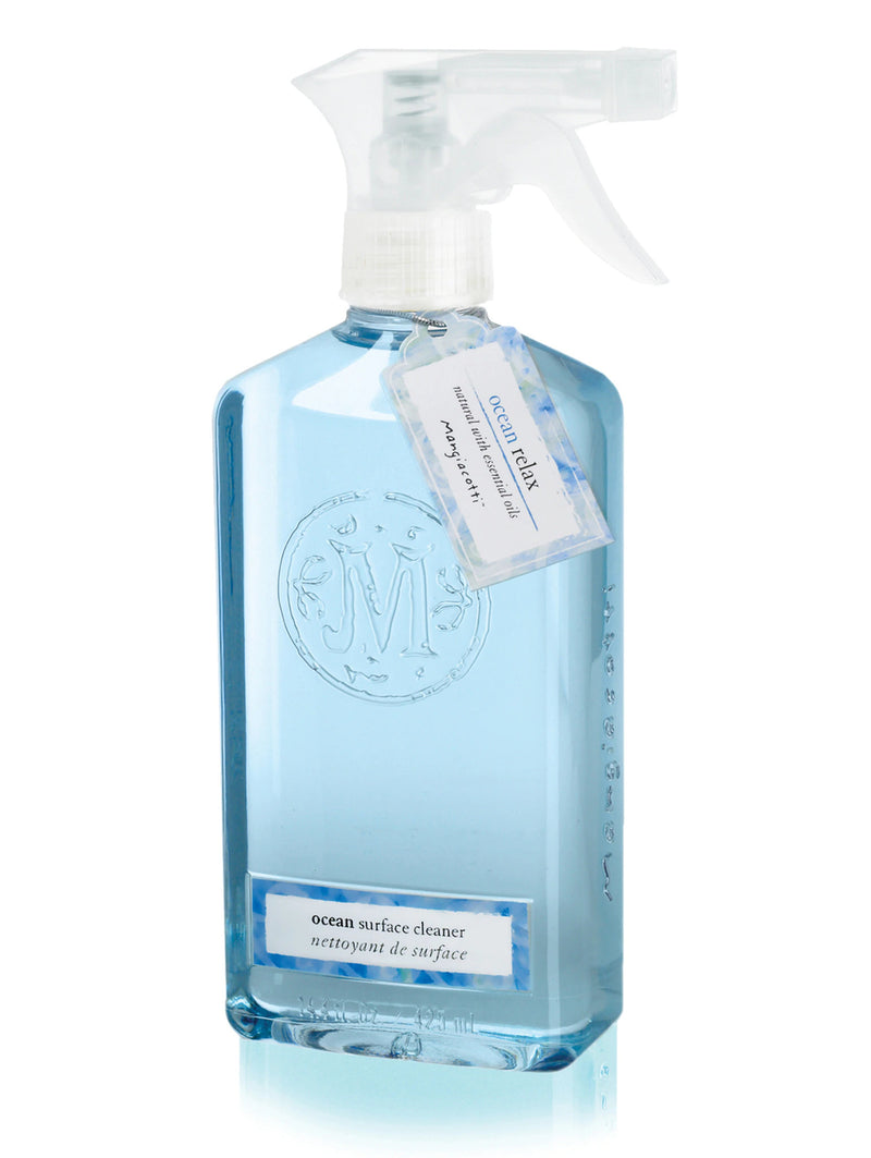 A transparent spray bottle containing blue liquid labeled "Mangiacotti Ocean Natural Surface Cleaner," with text both in English and French, featuring an embossed circular logo, designed for non-porous surfaces.