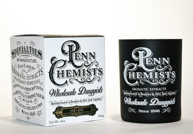 Two vintage-style Penn Chemists products: a white box labeled "wholesale druggists" featuring a Penn Chemists Classic Candle - Lady Day, and a black cylindrical container, both advertising aromatic extracts and dating back to.