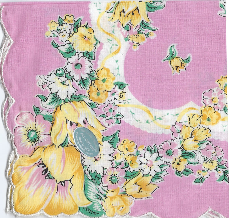 A vibrant Vintage-Inspired Hanky from Hankies ala Carte featuring large yellow and pink flowers on a pastel pink background, with a decorative scalloped white border and a "genuine hand print" label.