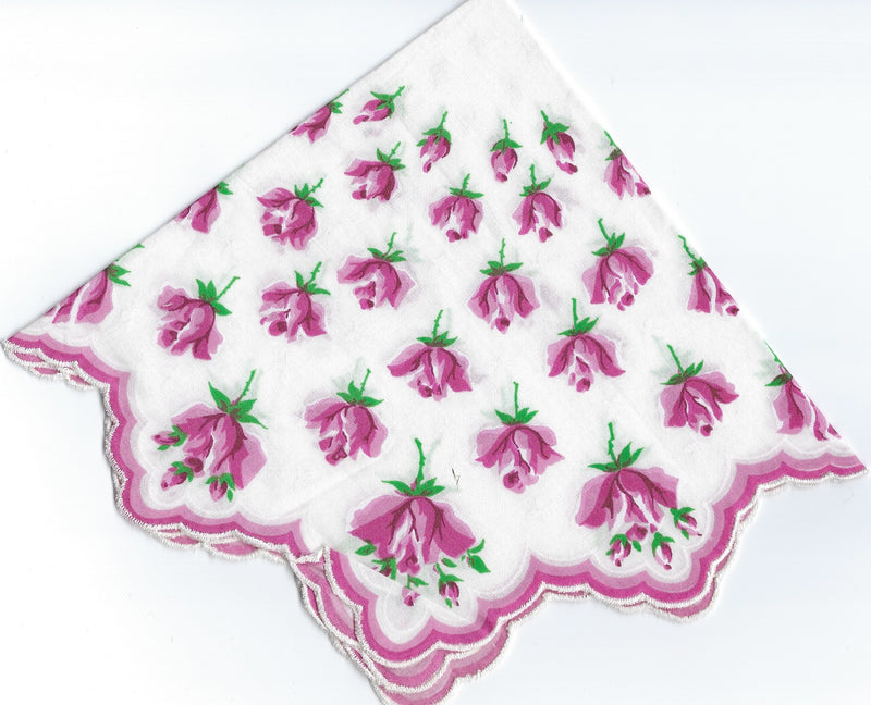 A square, white napkin with scalloped edges, decorated with multiple pink floral patterns and green leaves, displayed partially folded against a white background. This piece is reminiscent of Vintage-Inspired Hanky - Rosebuds to Rose Sprays Hanky by Hankies ala Carte.