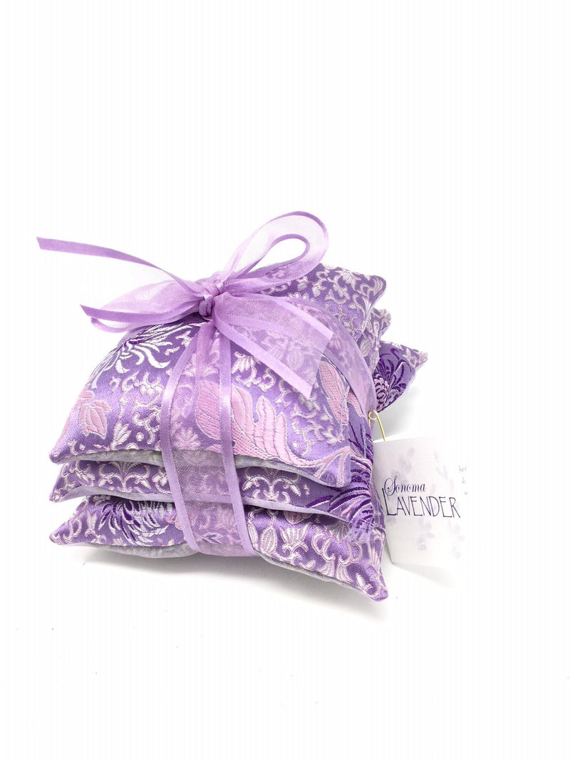 A stack of three purple Sonoma Lavender Sachet Trios tied with a light purple ribbon, featuring a delicate floral pattern and a label that reads "bohema lavender.