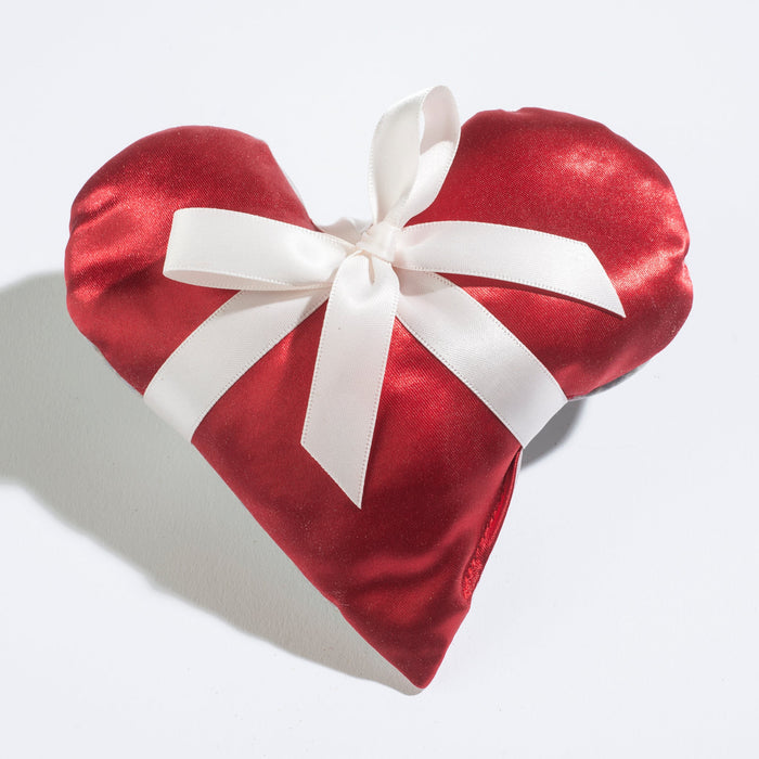 The Sonoma Lavender Heart Sachets - Red Satin is a limited edition, heart-shaped cushion featuring a shiny satin texture adorned with a large white bow at the center, casting a soft shadow on the light surface beneath it.