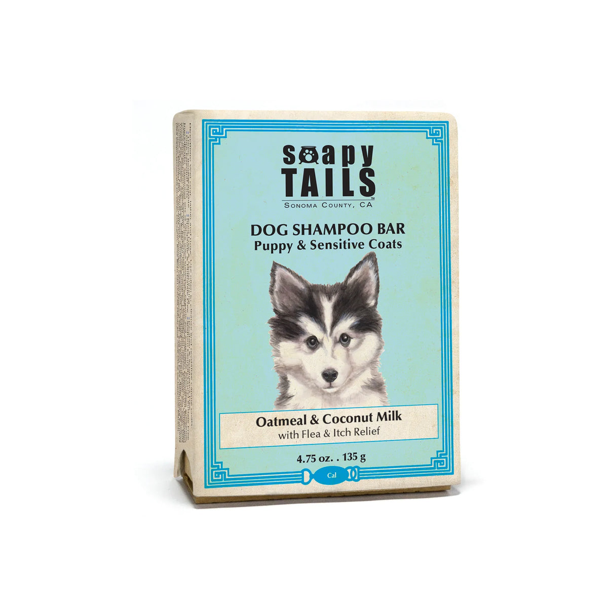 Packaging of the "Soapy Tails Shampoo Bar - Unscented Oatmeal & Coconut Milk- Fine Puppy & Sensitive Coats" by Three Sisters Apothecary featuring an image of a puppy on a teal background, with text detailing the product as suitable for puppies with sensitive coats and including oatmeal coconut milk.