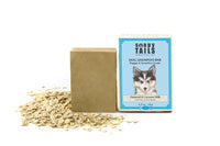 A Soapy Tails Shampoo Bar for puppies with sensitive coats and a flea relief formula, displayed next to a pile of dry oats, all set against a white background.