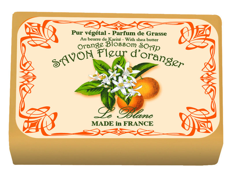 A bar of Le Blanc Orange Blossom Wrapped Soap with ornate label reading "savon fleur d'oranger, Le Blanc, handcrafted soap, made in France" alongside images of an orange and orange blossoms.