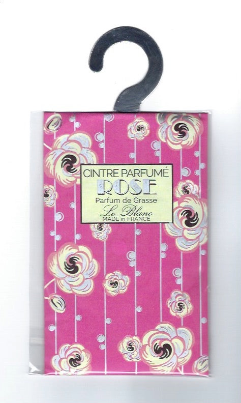A Le Blanc Rose scented hanging sachet in its packaging, featuring a vibrant pink background with white swirl designs and a black hook. The label includes text about the product's origin and fragrance from Grasse, France.