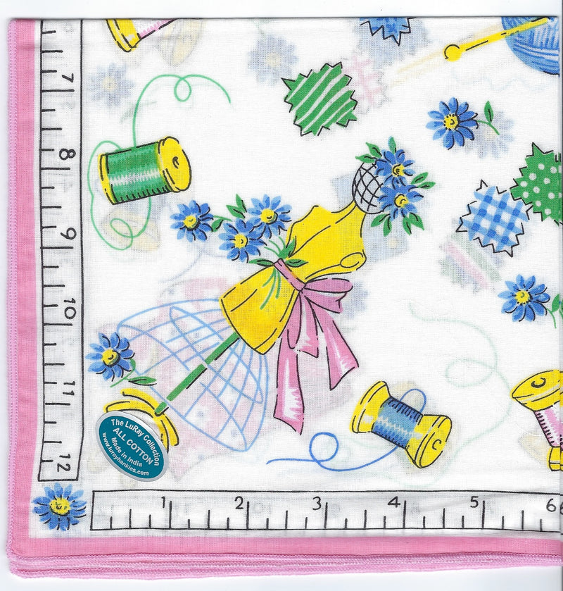 A vibrant fabric print featuring needlework motifs, including spools of thread, thimbles, and buttons intermixed with blue flowers. The left side includes a ruler for scale, highlighting measurements in centimeters.