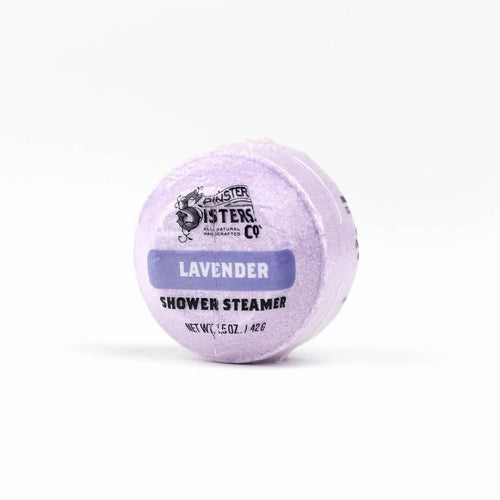 A lavender-colored shower steamer infused with lavender essential oil, labeled "Spinster Sisters Co. Lavender Shower Steamer" against a white background. The product weighs 1.5 oz.