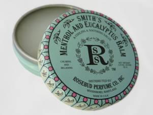 A round tin of Rosebud Perfume Co.'s Smith's Menthol and Eucalyptus Balm, marketed for alleviating cold sores, displayed open with its decorative green and pink lid featuring text and designs, resting