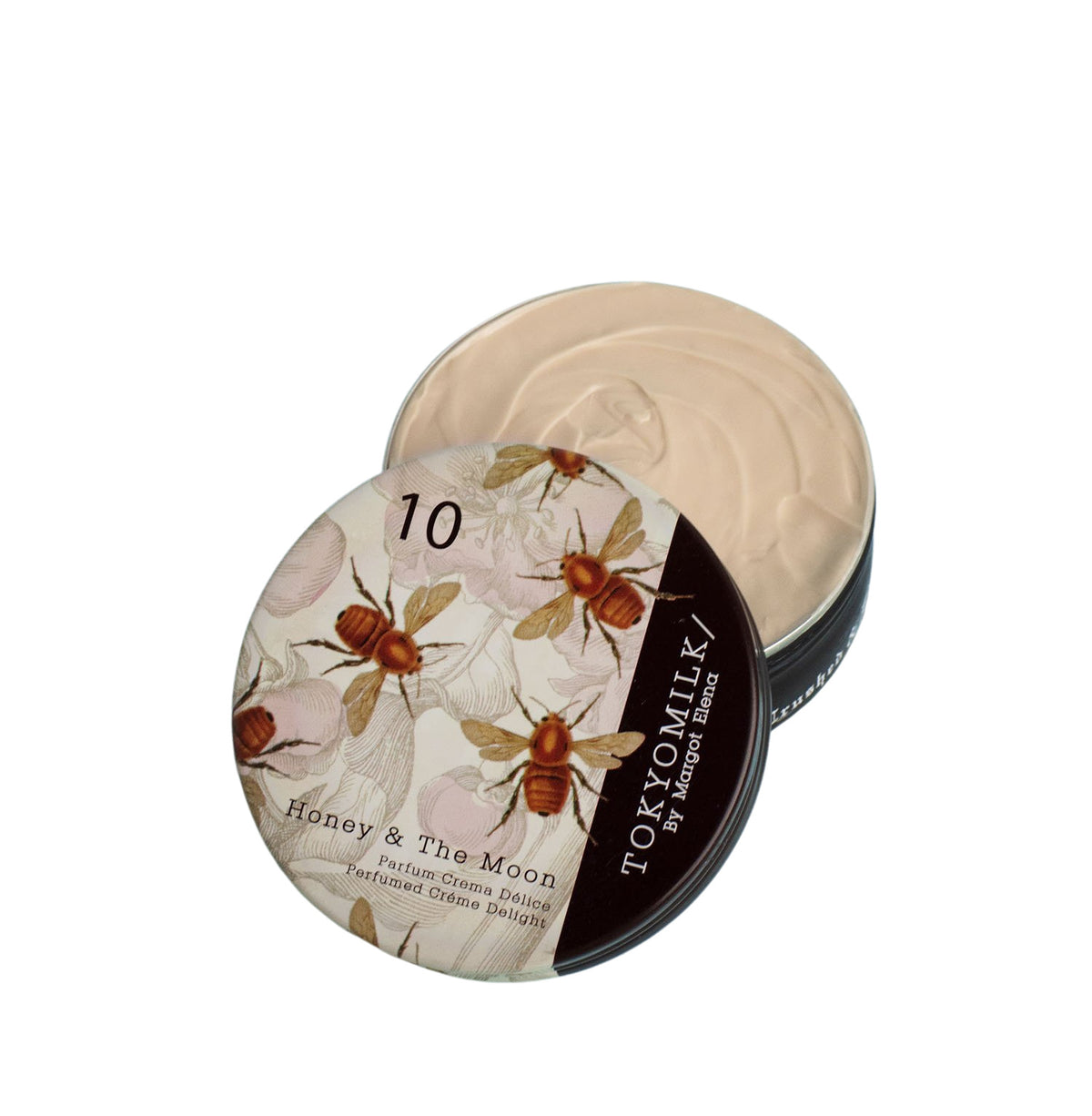 A round container of Margot Elena's TokyoMilk Honey & The Moon No. 10 Parfum Crema with a floral design on the lid, partially open to reveal a cream product inside.