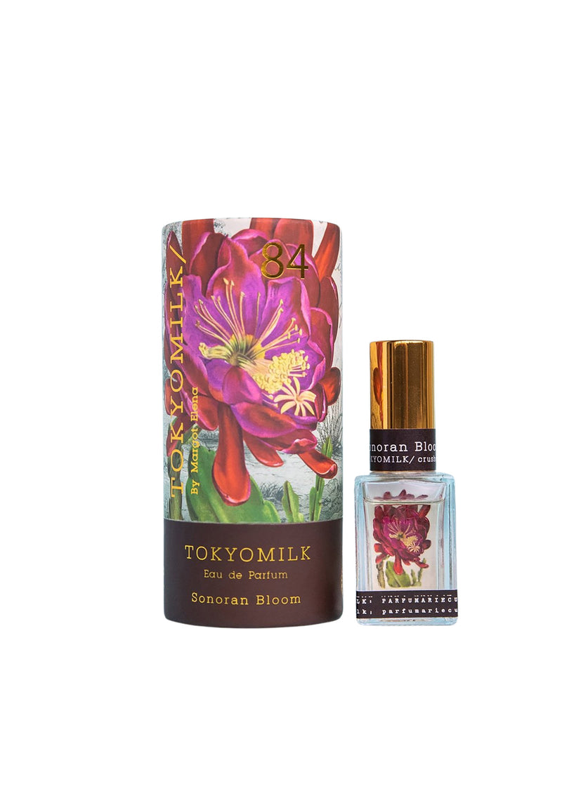 A bottle of Margot Elena's TokyoMilk Sonoran Bloom No. 83 Parfum next to its packaging, featuring vibrant floral artwork with deep red and saguaro flower on a white.