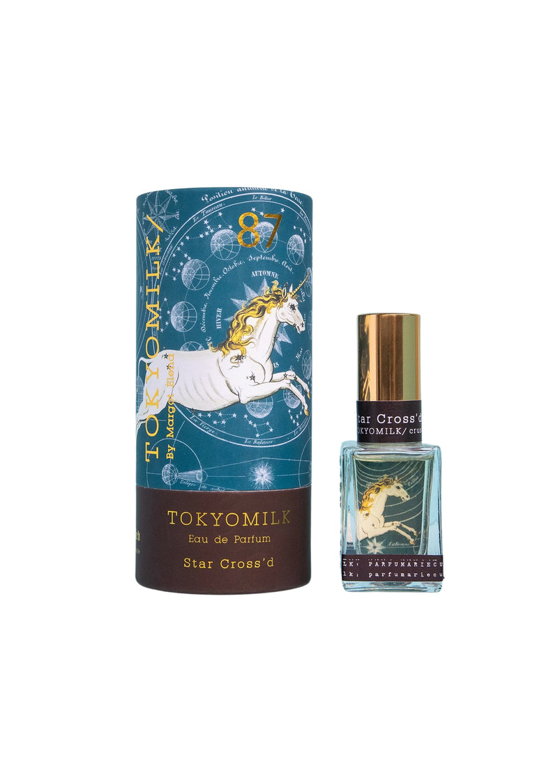 TokyoMilk Star Cross'd No. 87 Parfum by Margot Elena, with cylindrical packaging featuring a unicorn and celestial designs, displayed next to a glass perfume bottle with a matching label and infused with notes of water