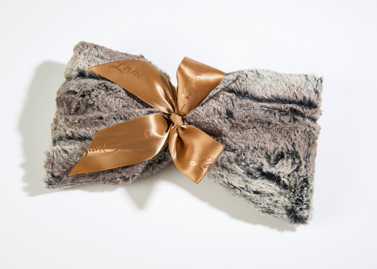 A soft, fuzzy gray Sonoma Timber Lake Woodland Fur Spa Mask tied with a golden satin bow, the bow displaying an embossed "love" text, laid against a white background alongside heated spa masks.