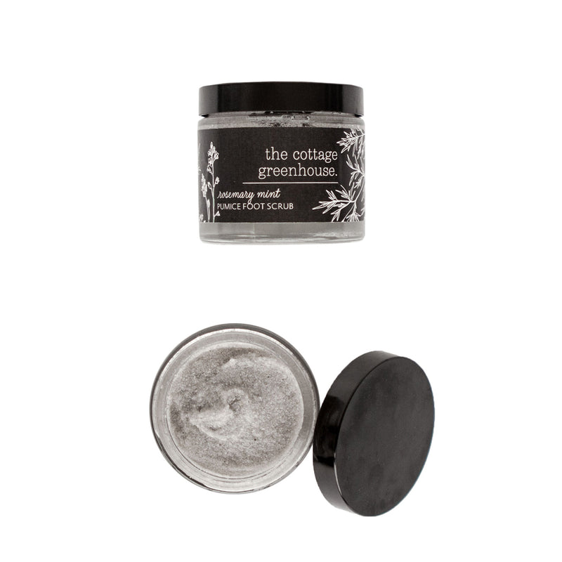 A jar of Margot Elena's "The Cottage Greenhouse Rosemary Mint Pumice Foot Scrub" with its lid off, showing the exfoliating scrub's texture, isolated on a white background.