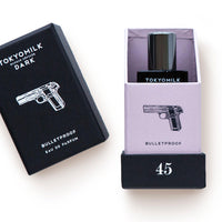 Two TokyoMilk Dark Bulletproof No. 45 Eau de Parfum products from Margot Elena. One box is black and the other lavender, each featuring a graphic of a pistol and labeled with the fragrance name "bulletproof," infused