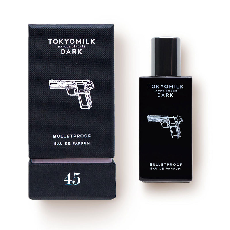 A product image featuring a black packaging labeled "Margot Elena's TokyoMilk Dark Bulletproof No. 45 Eau de Parfum" with a silver gun motif, beside an identical black perfume bottle with the.