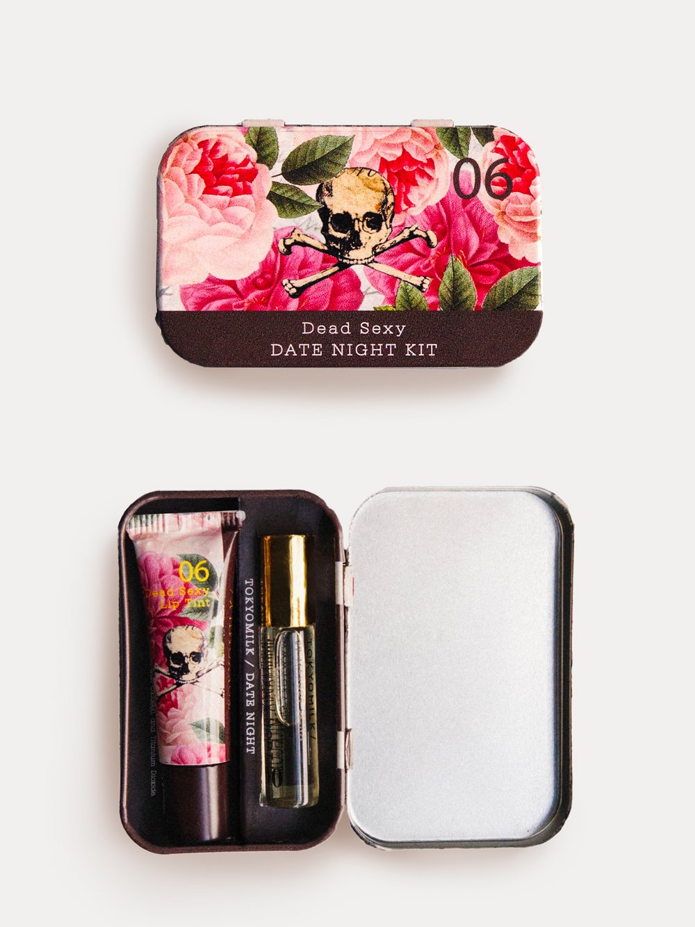 A "TokyoMilk Dead Sexy Date Night Tin Set" featuring a floral and skull design on the keepsake tin's cover. The open tin contains a rollerball parfum, breath spray, and lip tint from Margot Elena.