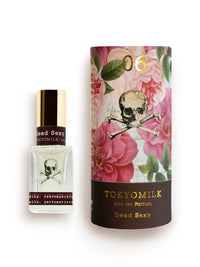 Two perfume bottles on a white background: a small glass bottle labeled "TokyoMilk Dead Sexy No. 6 Parfum" with a skull and bones design, featuring deep vanilla notes, and a larger cylinder with a floral and skull print, from Margot Elena.