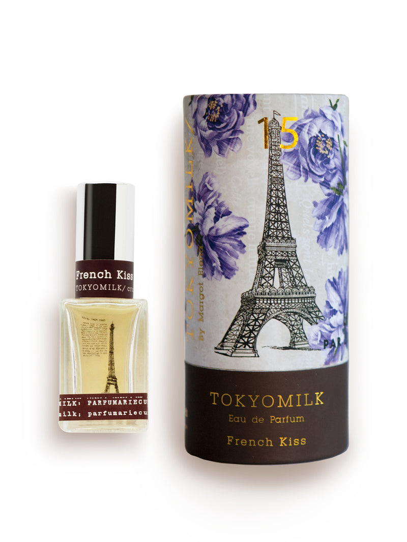 A bottle of Margot Elena TokyoMilk French Kiss No. 15 eau de parfum next to its packaging, featuring a design with the Eiffel Tower and gardenia flowers on a white background.