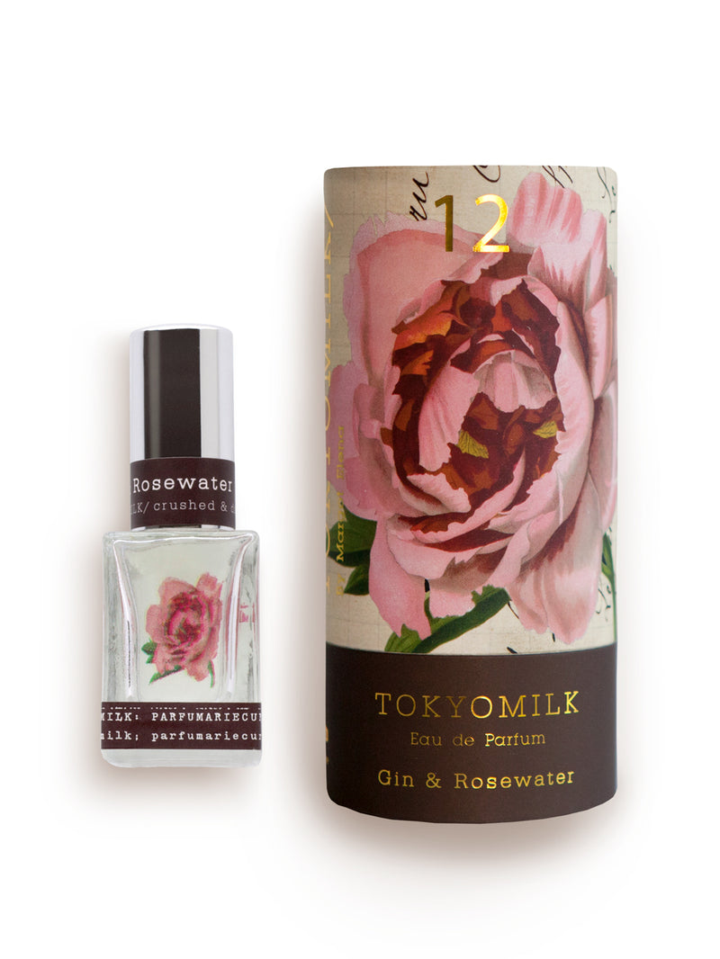 A bottle of Margot Elena's TokyoMilk Gin & Rosewater No. 12 Parfum next to its packaging, which features a large pink rose on a vintage-style label enhanced with hints of citrus zest.