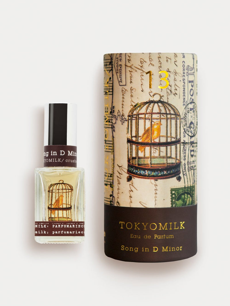 A bottle of Margot Elena's TokyoMilk Song in D Minor No. 13 Parfum, featuring notes of Gardenia, next to its packaging. The packaging has an artistic design with a bird in a cage and musical notes.