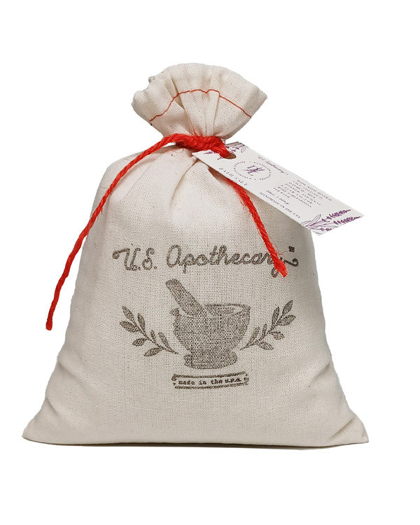A beige canvas drawstring pouch with a red tie featuring the printed words "U.S. Apothecary" and an image of a mortar and pestle adorned with lavender. A tag attached indicates U.S. Apothecary Dandelion & Lavender Bath Soak Bag.
