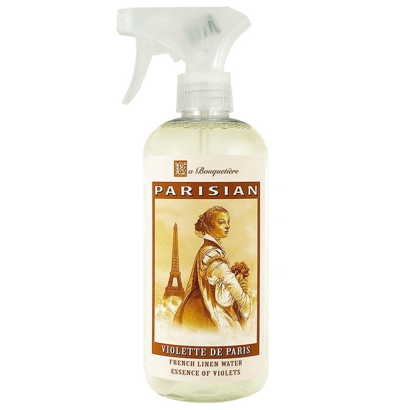 A clear spray bottle labeled "La Bouquetiere Violette de Paris French Linen Water, essence of violets", featuring a vintage illustration of a woman holding flowers with the Eiffel Tower.