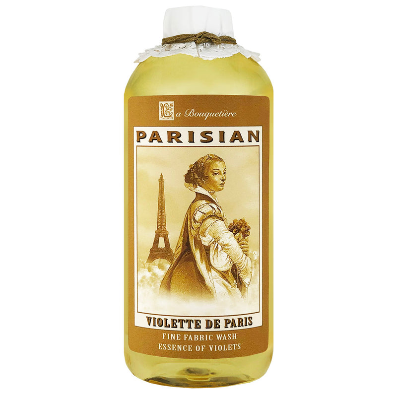 A bottle of French liquid detergent labeled "La Bouquetiere Violette Fine Fabric Wash" featuring an illustration of a woman in historical dress holding flowers with the Eiffel Tower in the background.
