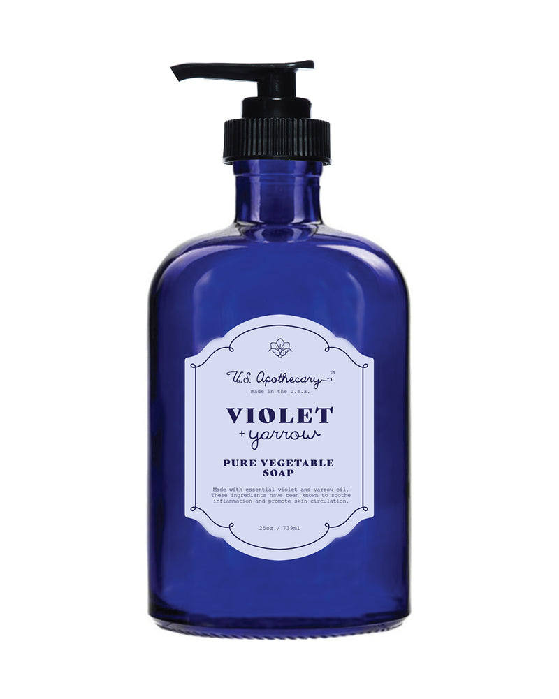 A blue glass bottle with a black pump labeled "U.S. Apothecary - Violet + Yarrow Liquid Soap" against a white background.