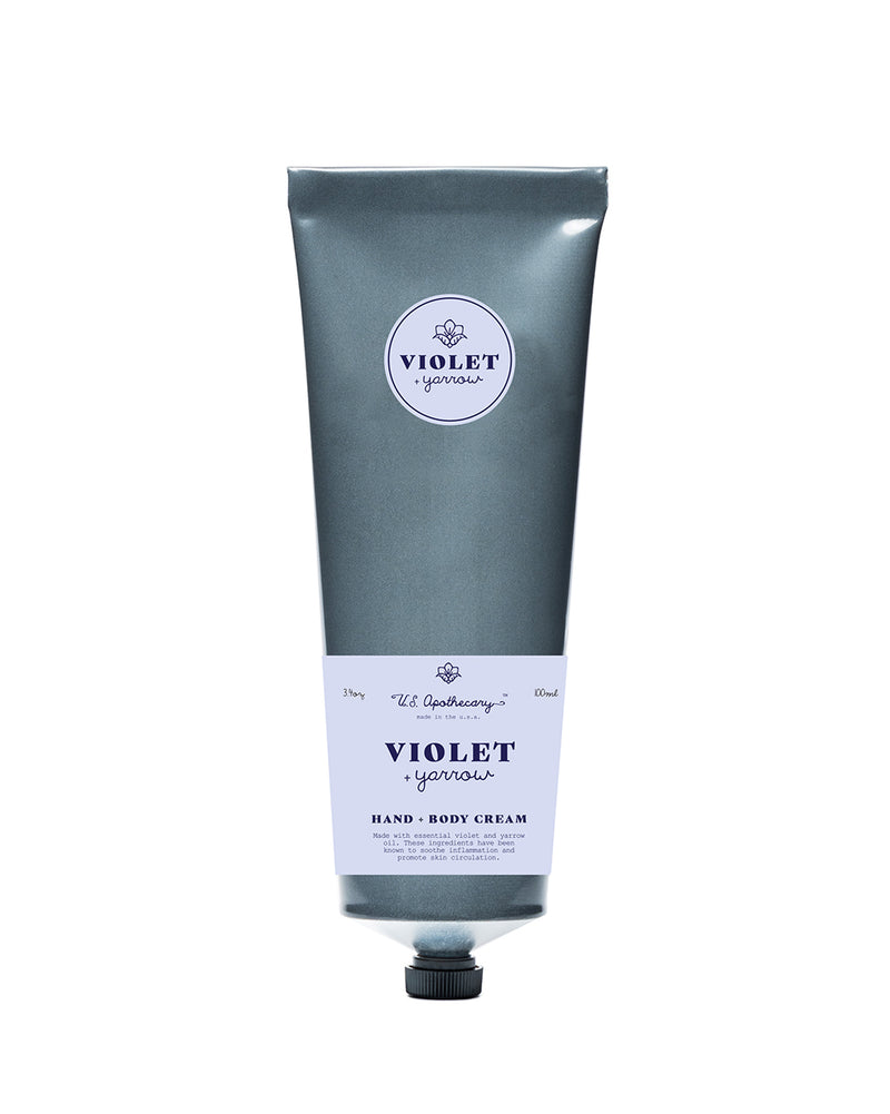 A tube of U.S. Apothecary Violet + Yarrow Hand & Body Cream, featuring sleek silver packaging with elegant white and purple text, and renowned for its moisturizing qualities.
