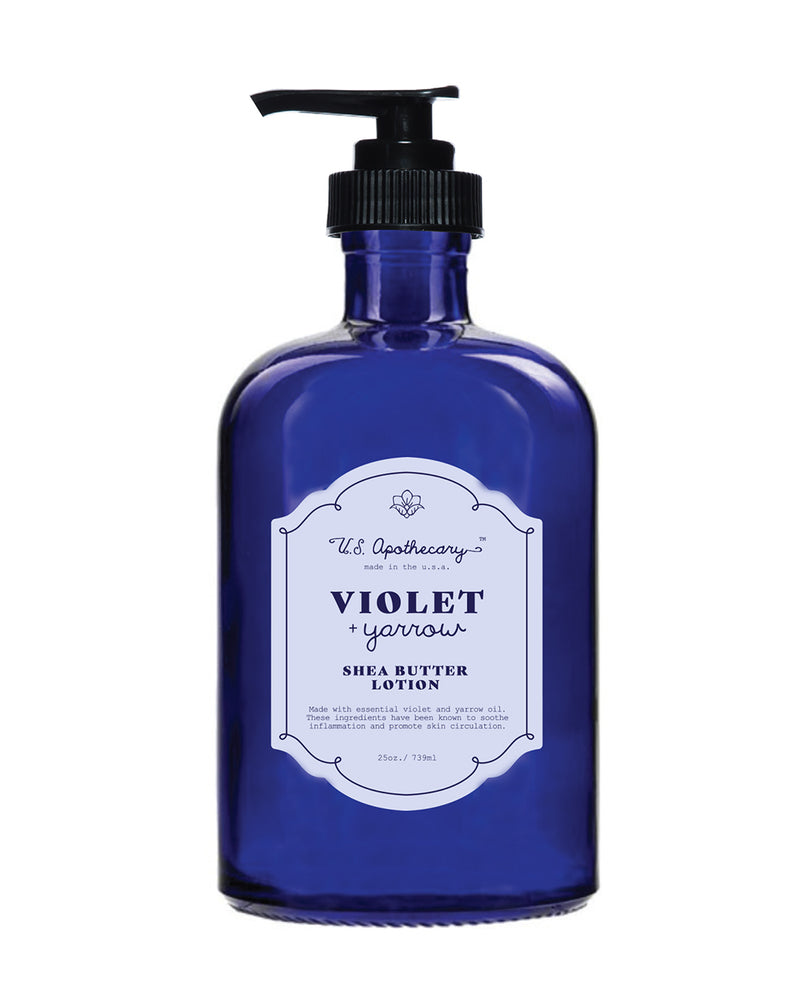 A cobalt blue glass bottle with a pump dispenser, labeled "U.S. Apothecary Violet + Yarrow Lotion." The label is white with elegant, vintage-style typography.