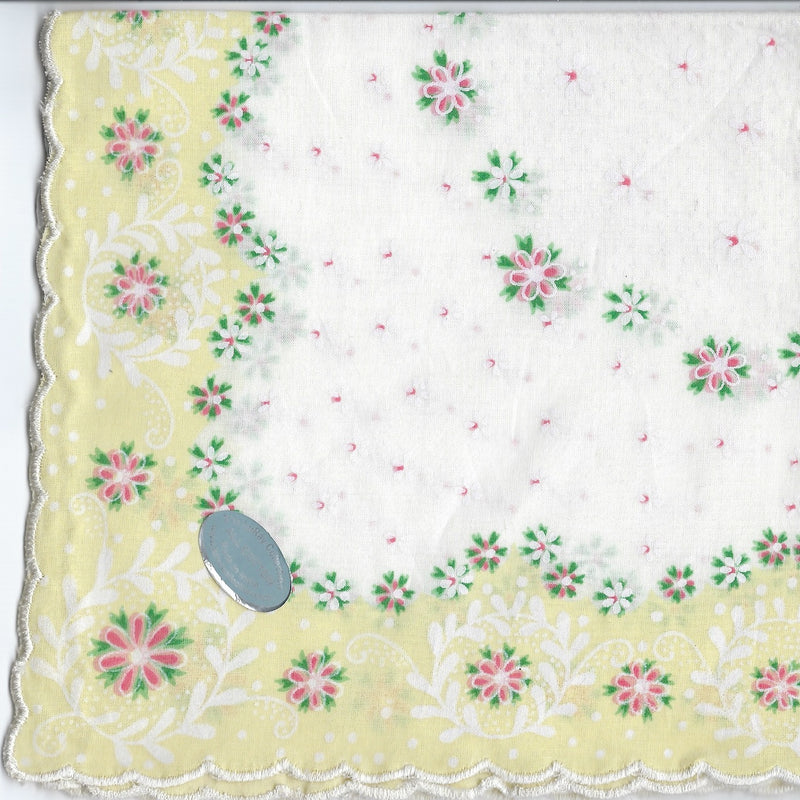 A scanned image of a Vintage-Inspired Hanky - Yellow Border with Petite Flower Design from Hankies ala Carte, featuring green vines and pink flowers. There is a scalloped edge and a grey oval object on the fabric made of pure cotton.