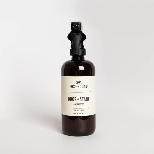 A brown spray bottle labeled "Fox + Hound -Odor with Stain Remover - Almond" on a white background. The label is simple, and the bottle has a black spray nozzle.