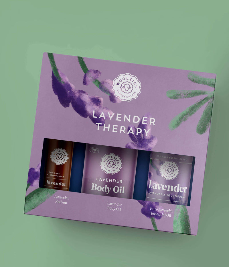 A set of Woolzies Lavender Therapy Kit products, including oils and a roll-on, packaged in a purple box with lavender plant illustrations on a muted green background.