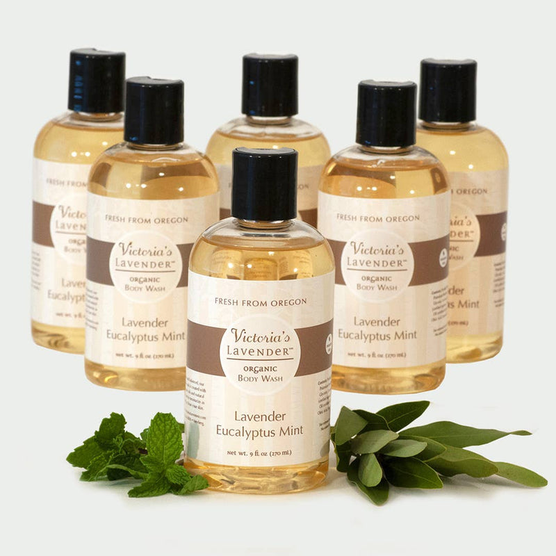 Five bottles of Victoria's Lavender Lavender Eucalyptus Mint organic, sulfate-free body wash, labeled "fresh from Oregon," are displayed with a sprig of fresh mint in the foreground.
