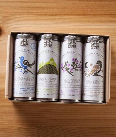 A Flying Bird Botanicals Herbal Lovers Gift Box containing five neatly arranged herbal tea cans with biodegradable tea bags, featuring decorative labels with birds and nature themes on a wooden surface.