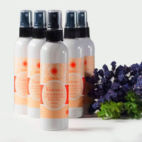 Four bottles of Victoria's Lavender After Sun Spray 4 oz "Cool It!" after sun spray, featuring lavender essential oil, with a focus on the front bottle. A bundle of lavender is beside them on a white background.