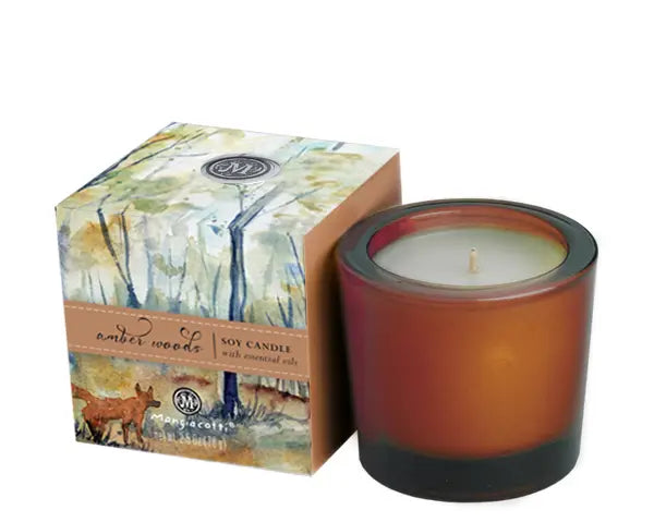 A Mangiacotti Amber Woods Soy Candle with an amber-colored wax in a brown glass holder, accompanied by its packaging featuring an abstract watercolor design and the label "amber woods.