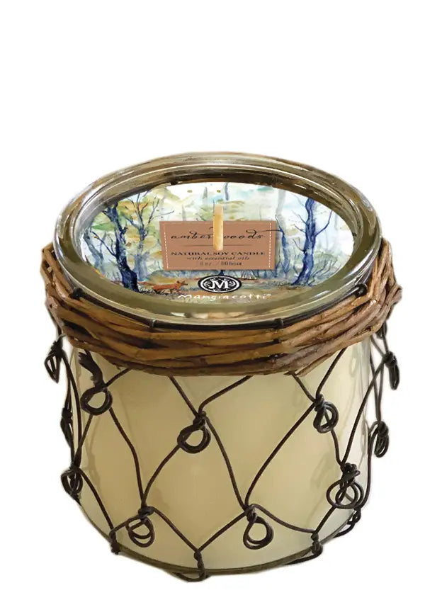 A Mangiacotti Amber Woods Farmhouse Soy Candle hand-poured in a glass jar, wrapped with a decorative metal wire and topped with a wooden lid featuring a tranquil forest scene on its label.