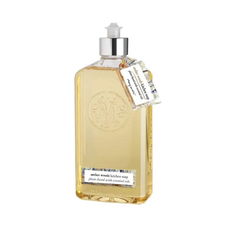 A transparent bottle of amber-colored Mangiacotti Amber Woods Kitchen Soap with a pump dispenser, enriched with essential oils and adorned with a tag featuring care instructions.